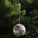 White and multi color round mosaic bird feeder hanging from a shepherd hook in the backyard.