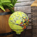 Yellow swirl gazing globe sitting in a gazing globe stand next to a brown faux wood planter.