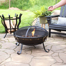 The spark screen of a black, Victorian style fire pit being removed by a fire poker.
