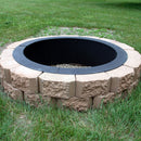A wood-burning fire pit liner is surrounded by bricks to create an above-ground fire pit in the grass.
