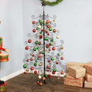 A metal Christmas ornament tree is decorated with red, green, and gold ornaments and displayed in a living room.