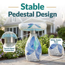 Mosaic Bloom Glass Bird Bath in indigo shown outdoors in a garden, featuring a secure bowl connection and a wide, stable pedestal base with blue, indigo, and aqua floral mosaic accents.