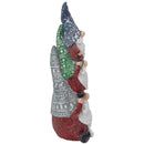 Side view of a stacked Christmas gnome statue showing the patterned blue, green, and gray hats, red clothing, white beards, and black shoes on a white background.
