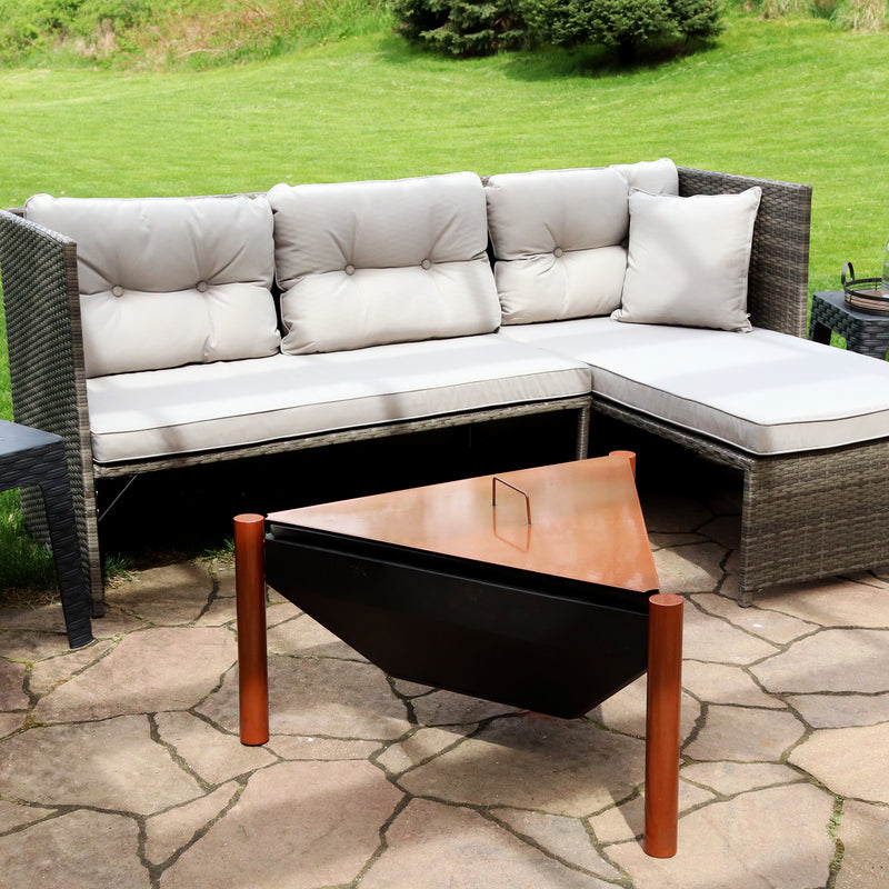 Triangle fire pit with copper legs and copper lid with handle sitting in front of a gray sofa with chaise lounge.