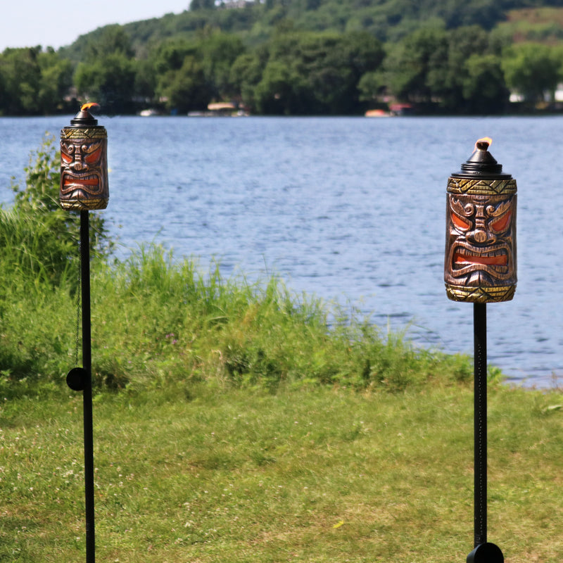 Tiki face citronella outdoor torches with burning wicks by the lake.