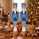 Two blue and gold nutcracker soldiers standing in a festive living room beside a decorated Christmas tree, surrounded by wrapped presents, a rocking horse, wooden toy train, teddy bear, and other holiday toys.