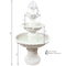 A white tiered outdoor fountain features a fruit design on top and has water pouring down the tiers in the yard.
