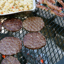 Four hamburgers cooking on a x-marks grill over a open fire.