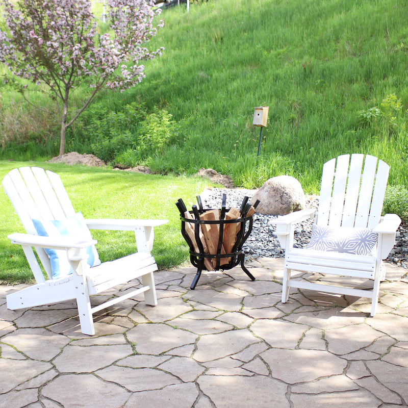 Two white Adirondack chairs with throw pillows on a stone patio with a modern fluted log holder between the chairs.