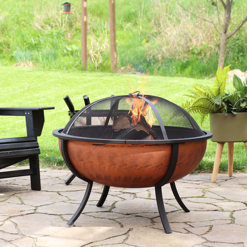 Lit copper-colored fire pit with spark screen on a stone patio.