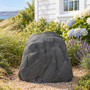 Dark gray faux rock cover with a realistic textured stone finish placed in a landscaped gravel garden bed surrounded by ornamental grasses, lavender, and blooming hydrangeas beside a white house.