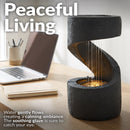 Black tabletop fountain with a curved cascading design and warm built-in lighting, shown on a desk creating a calming indoor ambiance.