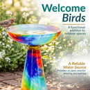 Vibrant multicolored glass birdbath filled with water, with a bird perched on the edge. Text highlights welcoming birds and providing a reliable water source for drinking and bathing.