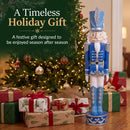 Blue Kristoff Christmas Nutcracker shown beside a decorated Christmas tree and wrapped gifts, highlighting a festive holiday gift designed to be enjoyed season after season.