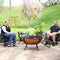 Woman and man sitting on black Adirondack chairs around a lit, copper-colored fire while the spark screen rests on the left-hand side.
