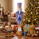Purple, blue, white, and gold Christmas nutcracker displayed indoors beside a decorated Christmas tree, surrounded by wrapped gifts, a rocking horse, toys, and a teddy bear.