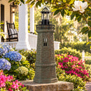 Weathered brown and green lighthouse statue displayed on a brick garden wall surrounded by blue hydrangeas, pink flowers, and greenery in a landscaped front yard.