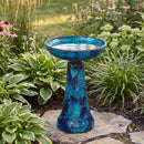 Crackled Glass Mosaic Bird Bath in deep ocean swirl shown in a landscaped garden, featuring a shimmering blue and turquoise crackled glass bowl and tapered pedestal filled with water.