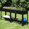 Two black raised garden beds placed outside, side by side, full of colorful flowers and plants.