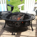 Large fire pit with outer ring on a stone patio patio, behind it is one black and one white Adirondack chairs.