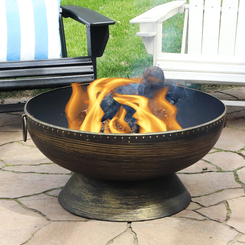 Brass-colored contemporary-style fire sits on stone patio with two Adirondack chairs behind it.