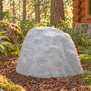 Light gray decorative faux rock cover with a tall, tapered shape and realistic stone texture, placed in a mulch-covered forest landscape surrounded by ferns, trees, and a rustic log cabin.