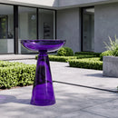 Purple glass birdbath displayed on a modern outdoor patio, surrounded by manicured greenery and contemporary landscaping.