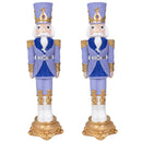 Two purple and blue Christmas nutcracker statues with gold accents, white beards, ornate uniforms, and decorative gold bases displayed side by side against a white background.