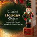 Traditional Christmas nutcracker decoration dressed in a red, green, and gold uniform, holding a festive wreath and candy cane while standing on a Merry Christmas base. Displayed beside a cozy brick fireplace with warm holiday lighting, highlighting its classic holiday charm and festive character.
