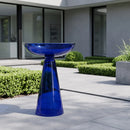 Blue glass birdbath displayed on a modern outdoor patio, surrounded by manicured greenery and contemporary landscaping.