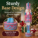 Pink Kristoff Christmas Nutcracker shown beside a decorated Christmas tree and wrapped gifts, featuring a sturdy decorative base designed for stable placement on flat surfaces.