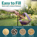 Modern Mosaic Fly-Through Bird Feeder in iridescent purple shown being filled with birdseed in a garden. Open design makes filling easy and works with millet, sunflower, safflower, and mixed seed.