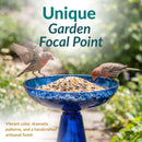 Blue glass birdbath filled with birdseed, with two birds perched on the bowl. Text highlights its unique garden focal point, vibrant color, dramatic patterns, and handcrafted artisanal finish.