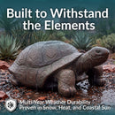 Weather-resistant decorative tortoise garden statue with a textured brown and green finish, shown on a lawn surrounded by rocks, shrubs, and flowers.