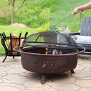 Bronze fire pit with star and moon cut outs having it's spark screen removed by a fire poker.