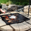 Square grilling grate with burger patties and hotdogs over a burning stone fire pit.