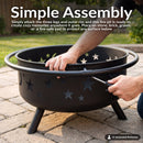 Black Cosmic Fire Pit shown during assembly on a stone patio, with a person securing the outer rim to the fire bowl using a screwdriver, highlighting the simple assembly process.