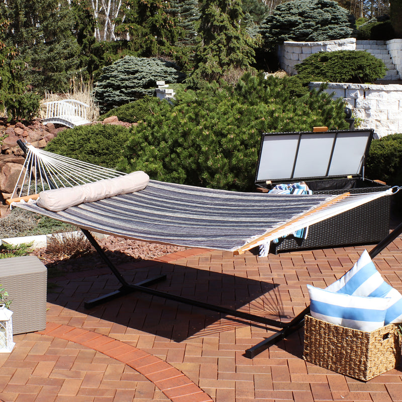 Blue and gray stripped hammock with a gray pillow pulled taught on a stand sitting on a stone patio.