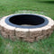 A wood-burning fire pit liner is surrounded by bricks to create an above-ground fire pit in the grass.
