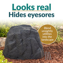 Dark gray faux rock utility cover with a realistic rugged stone texture displayed in a landscaped garden. Text highlights its natural appearance and ability to conceal unsightly utilities. Three metal ground stakes are shown beside the rock.