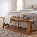 Sunnydaze Teak Trestle Bench at the foot of the bed with props on the top of the bench, the scene is showing a bright airy farmhouse inspired image
