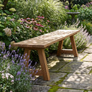 Sunnydaze Teak Trestle Bench in a garden setting with flowers around the bench and dappled sunlight