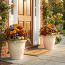 Two cream-colored decorative planters filled with vibrant autumn flowers displayed beside a front door and stone walkway.