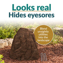 Infographic featuring a tall, tapered dark brown faux rock cover with a realistic stone texture in a mulched garden bed. Text reads “Looks real, Hides eyesores” with a callout explaining how it blends unsightly utilities into the landscape. Three metal ground stakes are displayed beside the rock.