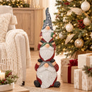 Stacked Christmas gnome statue displayed beside a decorated Christmas tree with wrapped gifts, warm lighting, and neutral holiday décor.