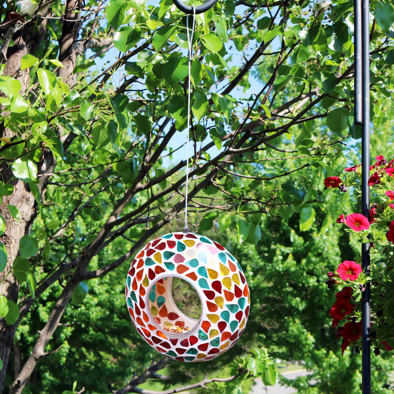 Mosaic fly-through hanging bird feeder filled with bird seed hanging from a tree.