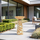 Tan and cream decorative pedestal bird bath displayed on a modern outdoor patio surrounded by landscaped greenery and contemporary seating.