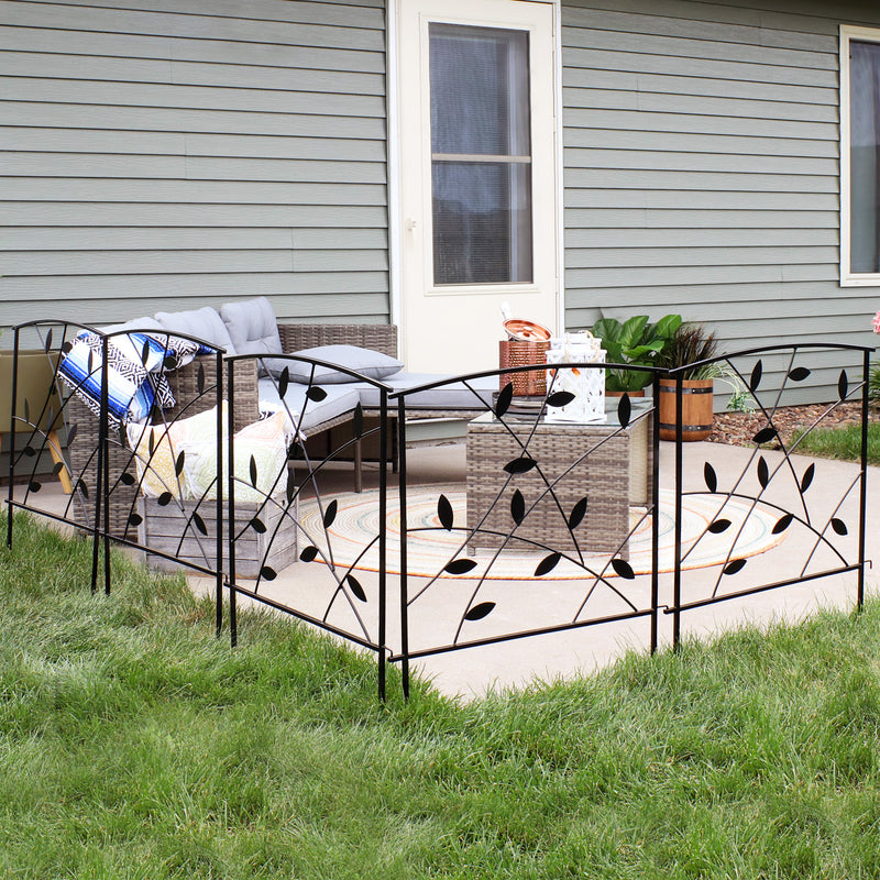 Modern 5-piece fence panels with decorative metal leaves placed in grass connected to create a border around a backyard patio.