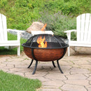A lit copper-colored fire pit spark screen being remove by a fire poker.