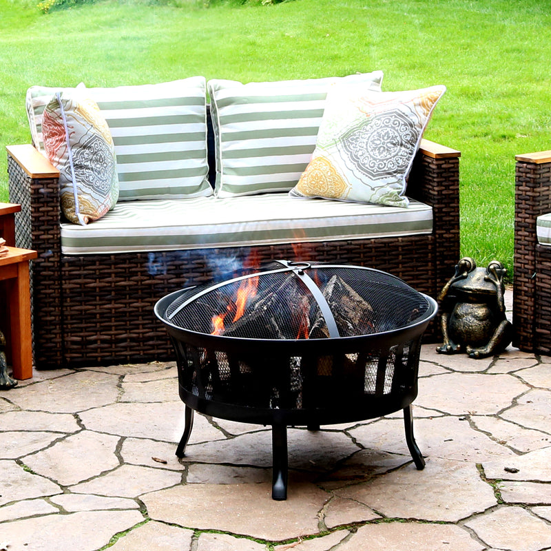 Mesh stripe cutout fire pit with fire burning sitting on a stone patio with patio furniture and pillows behind it 